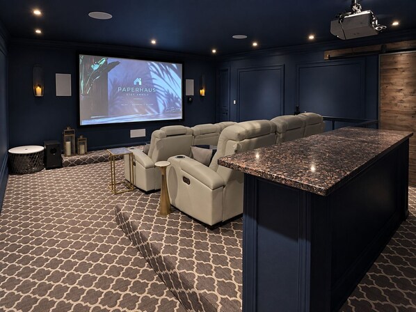 Un cine en casa con una pantalla grande, asientos cómodos y una pequeña zona de bar.