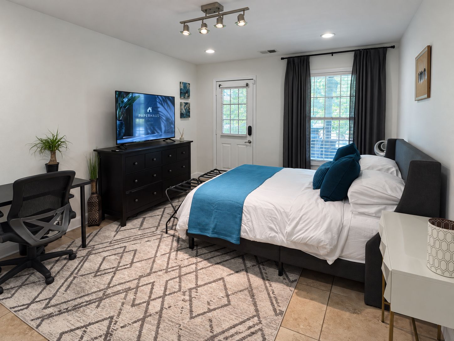 Un dormitorio moderno con cama, escritorio, televisor y ventana con cortinas.