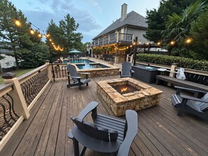 A deck with a fire pit, outdoor seating, and a pool area. - Saltwater Pool • Hot Tub • Movie Rm • 5BR Retreat (Lawrenceville)