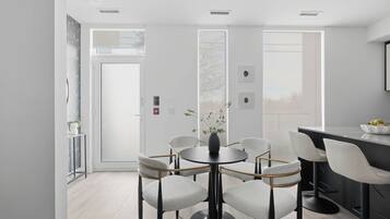 A modern dining area with a round table and six chairs, a kitchen area with a black countertop, and a door leading outside.