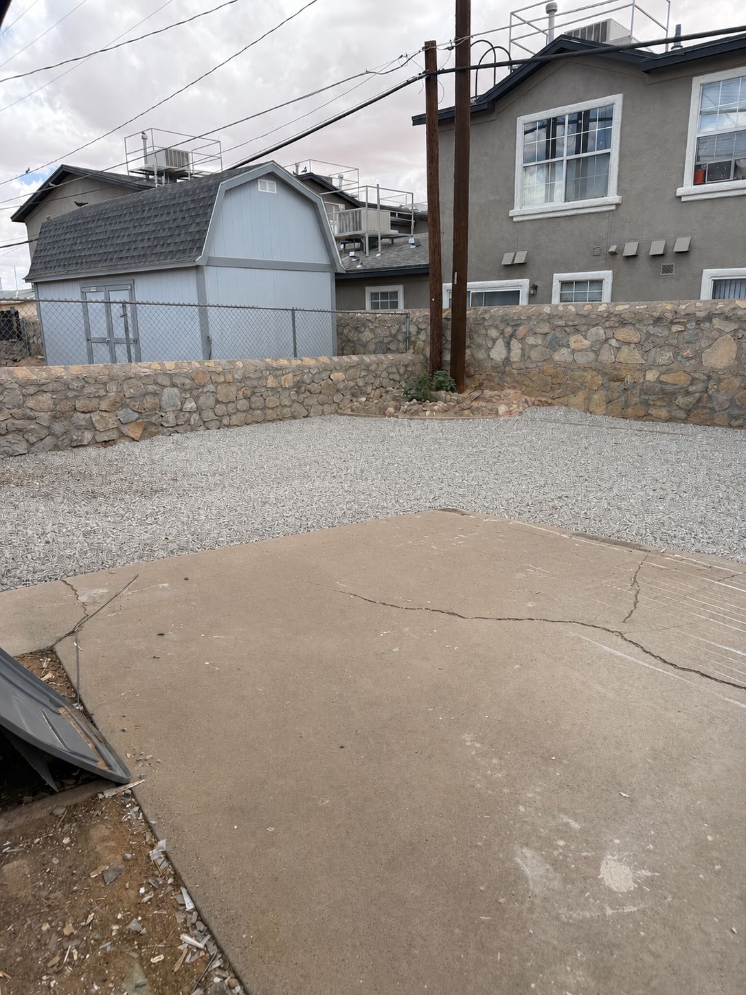 A residential area with a concrete patio, a stone wall, and a house with a grey facade and white windows.