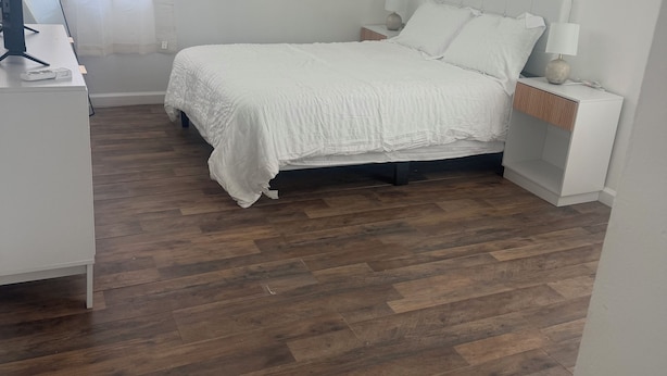 Un dormitorio con cama, mesitas de noche, un escritorio con computadora y una ventana con cortinas.