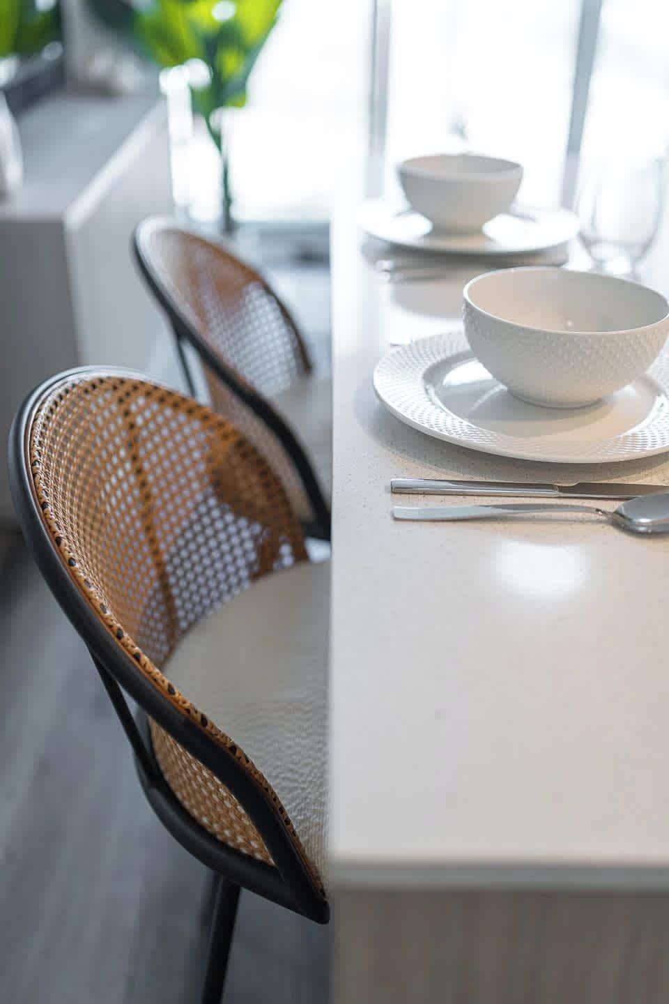 A dining area with a white table, two chairs with woven seats, and a white bowl on the table.