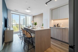 A modern kitchen with a central island, bar stools, and a view of the city through large windows.
