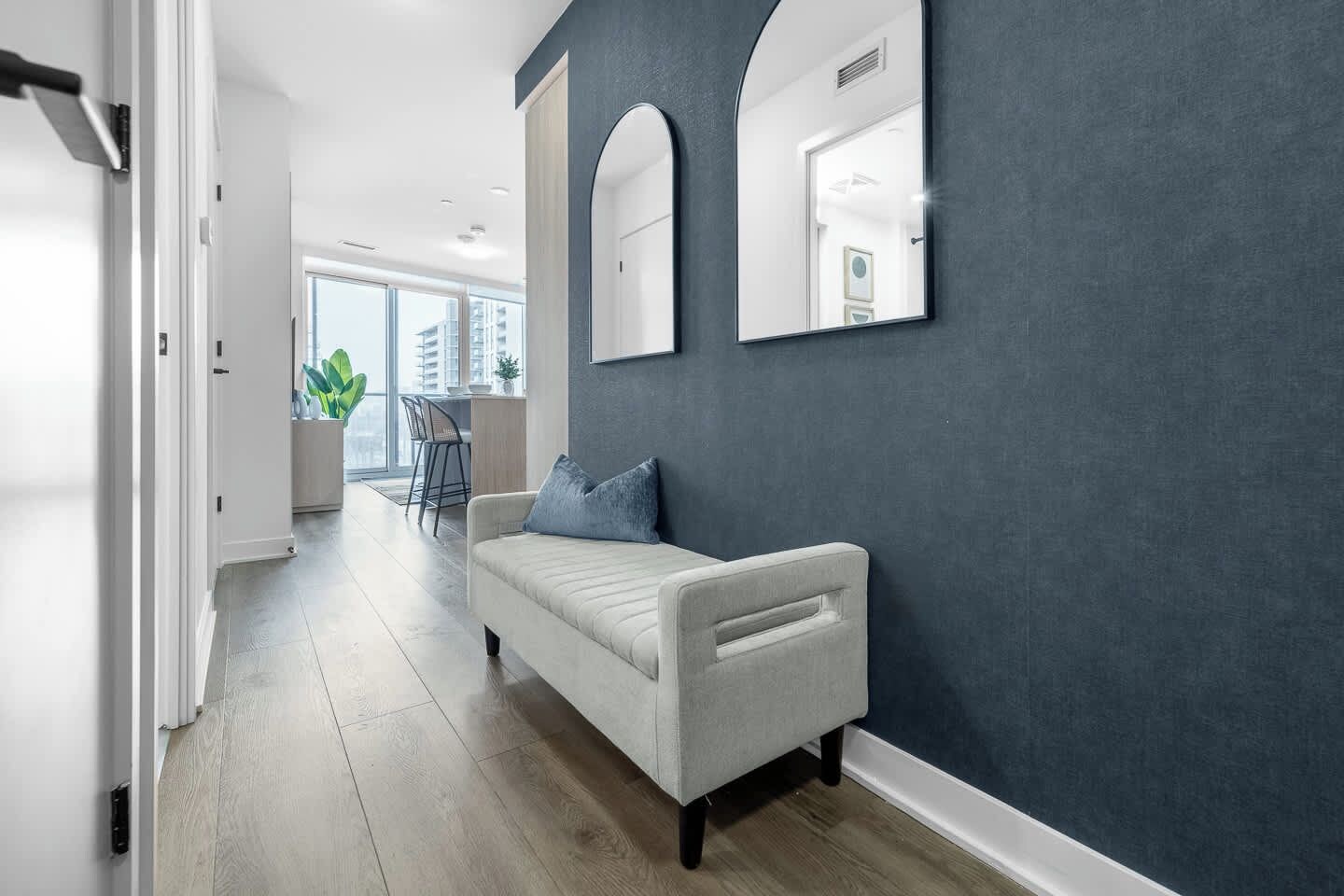 A hallway with a white sofa, dark wall, and a door leading to a bright room.