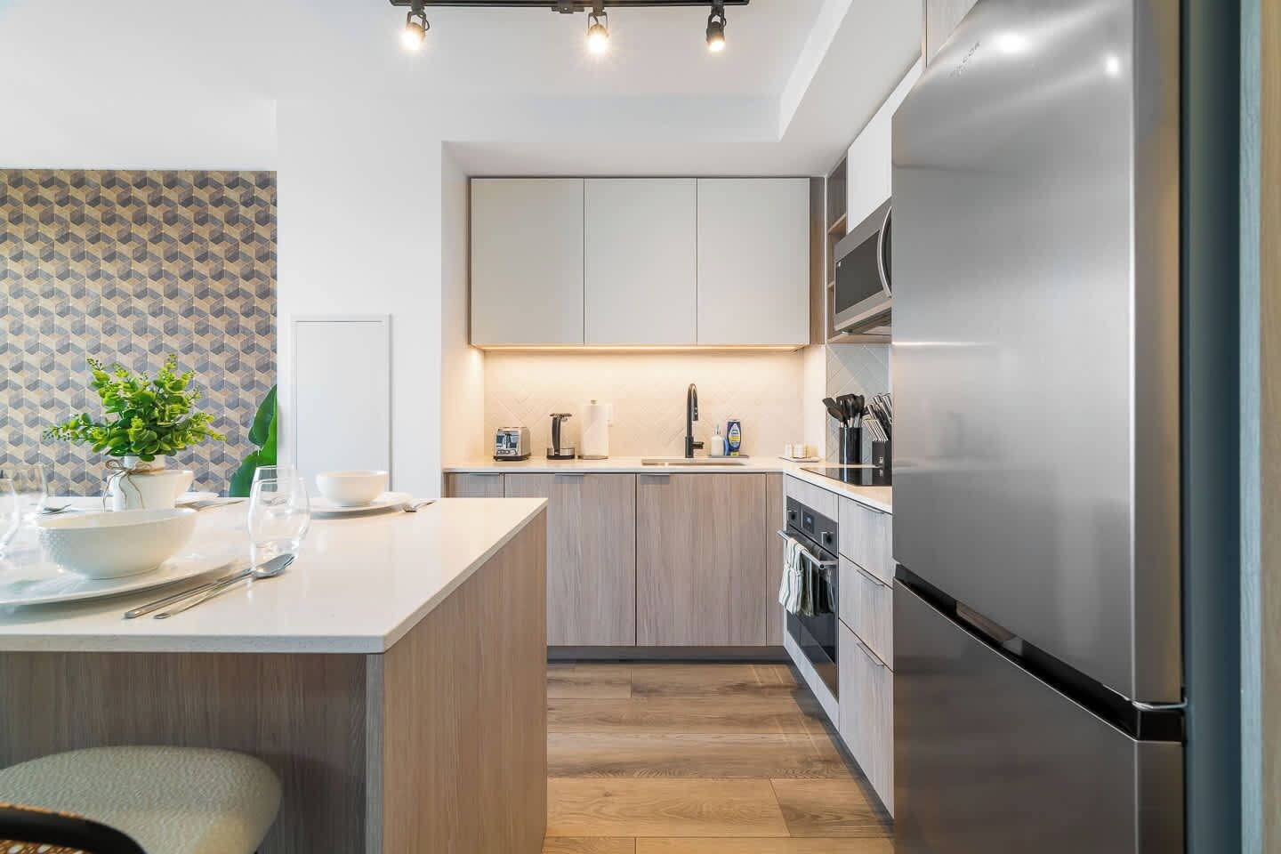 Una cocina moderna con una isla central, electrodomésticos de acero inoxidable y acabados en madera clara.
