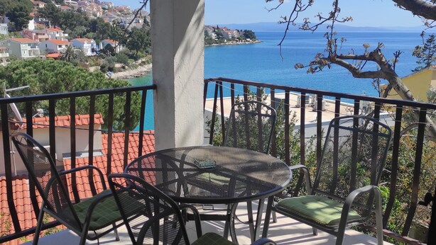 Ein Balkon mit Tisch und Stühlen, der Blick auf die Küste mit Gebäuden und einem klaren Himmel bietet.