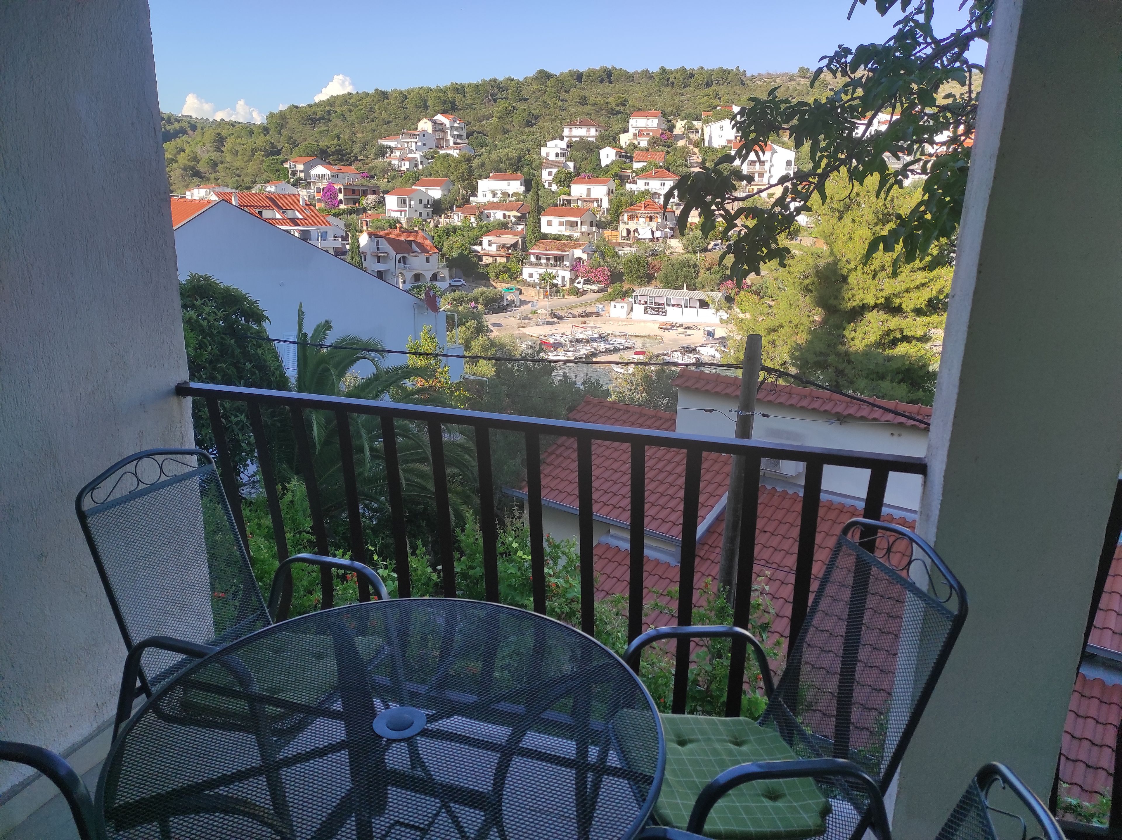 A balcony with a table and chairs, overlooking a hillside with houses and a marina.