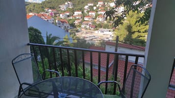 A balcony with a table and chairs, overlooking a hillside with houses and a marina.