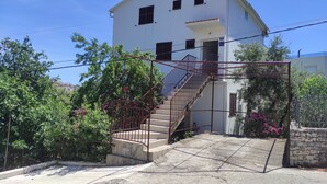 Ein weißes Gebäude mit einer Treppe, die zu einem Balkon führt, umgeben von Grünpflanzen und blühenden Blumen.