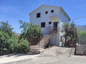 Un edificio blanco con una escalera que conduce a un balcón, rodeado de follaje y plantas en flor.