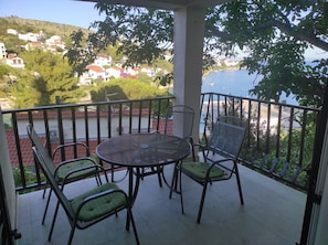 Un balcón con mesa y sillas, con vistas a la costa, edificios y árboles.