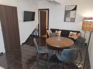 A dining area with a round table, four chairs, a television mounted on the wall, and a floor lamp.