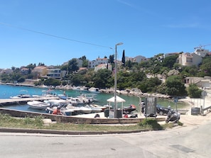 Una marina costera con barcos amarrados, un paseo peatonal y edificios residenciales al fondo.