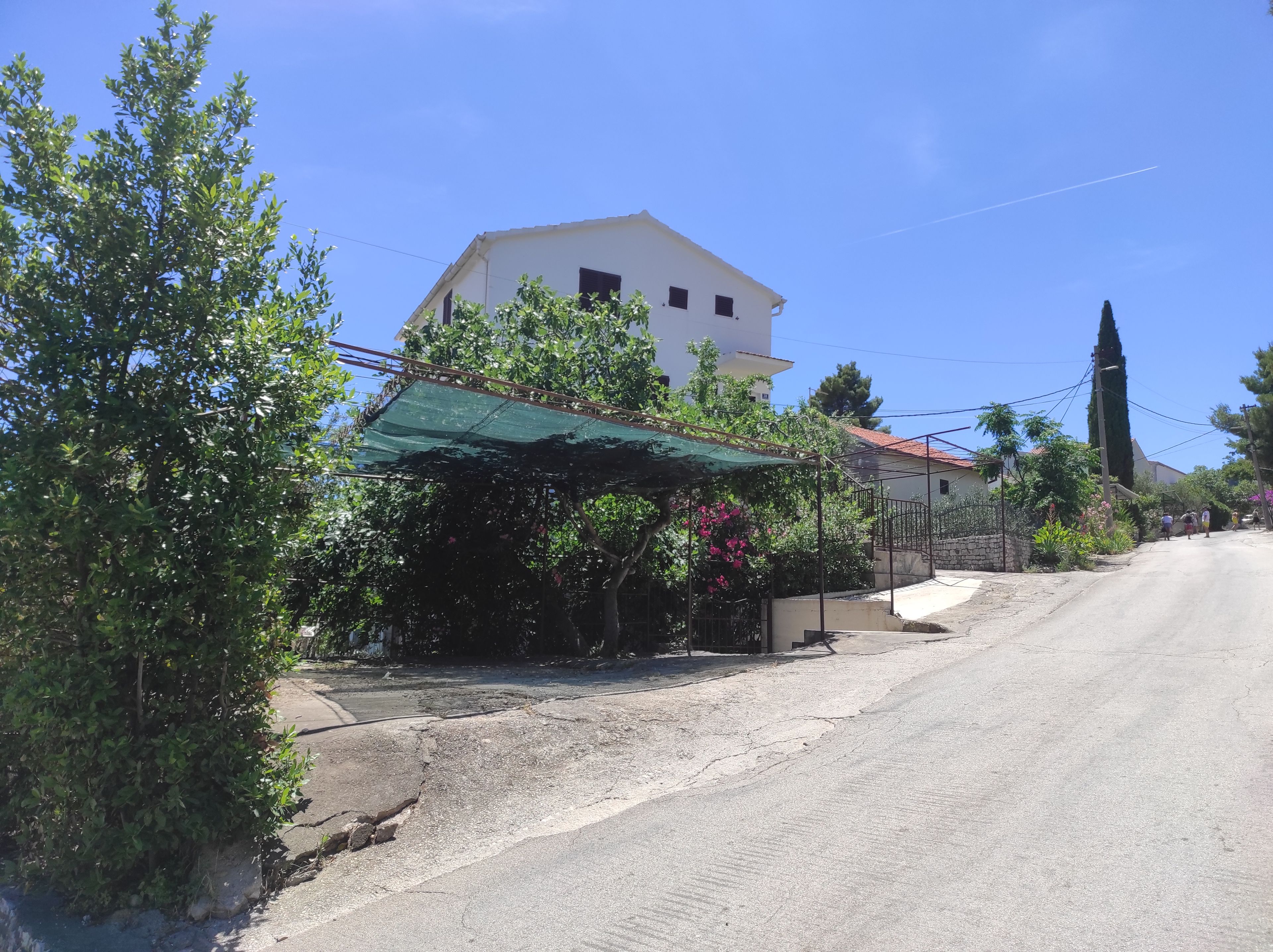 Une rue résidentielle avec une maison blanche, un auvent vert et un ciel bleu dégagé.
