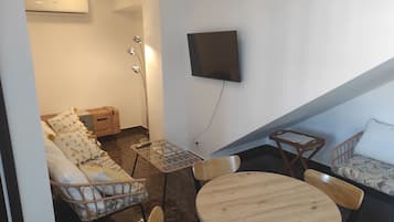 A living room with a sofa, chairs, a table, a TV mounted on the wall, and an air conditioning unit.