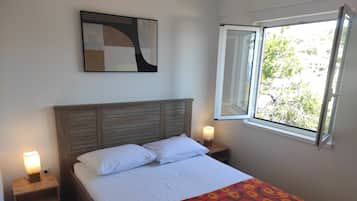 A bed with a patterned bedspread, a wooden headboard, two bedside lamps, and a window with an open view.