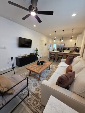 A modern living room with a sofa, coffee table, and a TV mounted on the wall. - 2-bedroom home w/AC, Enjoy your Stay at the Urban Nest, 7 Mins to Downtown (San Antonio)