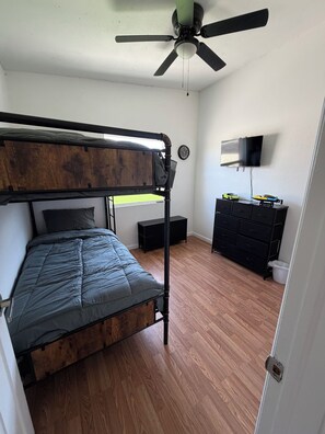Quarto com beliche, ventoinha no teto, televisão e cômoda.