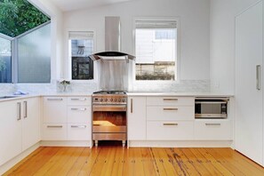 A modern kitchen with white cabinetry, a stainless steel range hood, a built-in oven, and a microwave. - Grafton Garden 4BR Retreat near Domain (Auckland CBD)