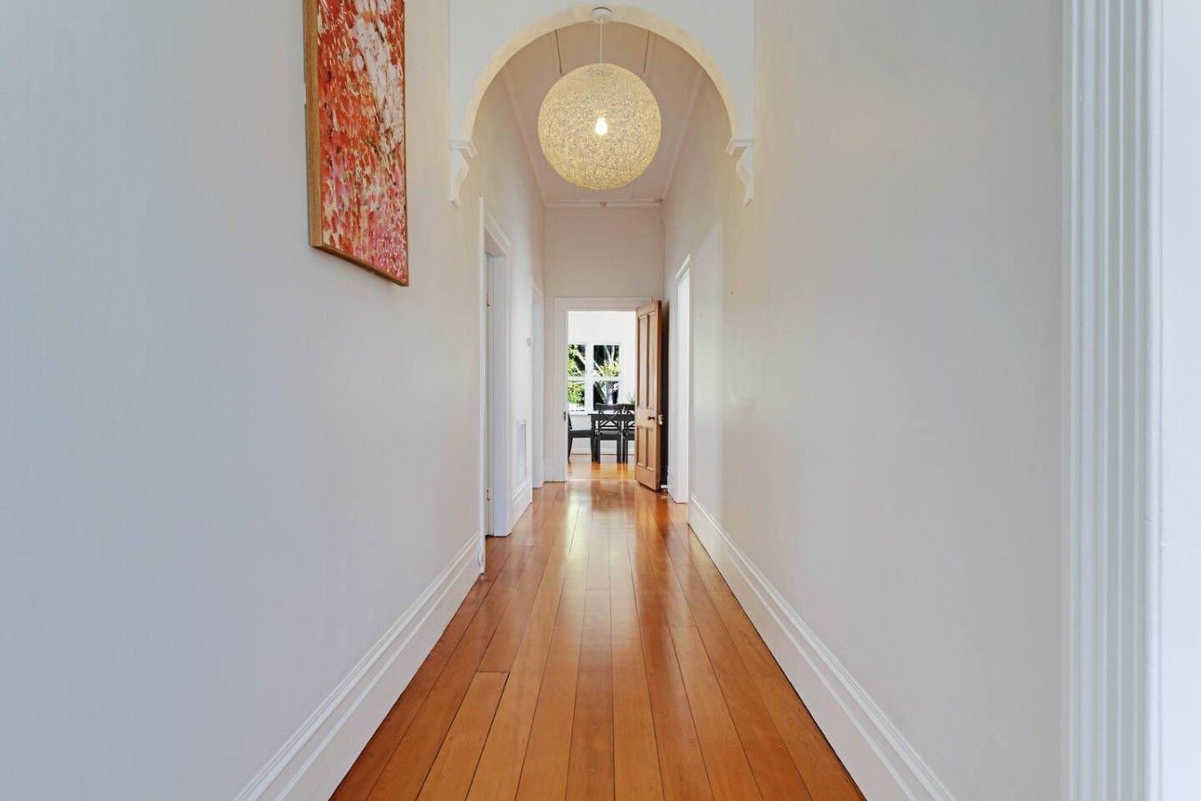 A hallway with wooden flooring, white walls, and a ceiling light fixture.