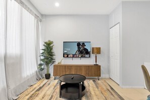 Un salon avec un téléviseur à écran plat fixé au mur, une table basse ronde, une plante en pot et un meuble en bois.