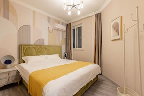 Une chambre d’hôtel comprenant un lit, une table de chevet, une lampe, un appareil de climatisation, une fenêtre, des rideaux et un tableau encadré au mur.