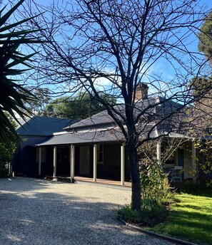 Ein Haus mit einer Veranda, einer Schotterauffahrt und einem Baum im Vordergrund.