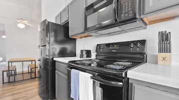 Una cocina moderna con un refrigerador negro, un microondas de acero inoxidable y una estufa negra. Hay una mesa de madera con sillas y un ventilador de techo.