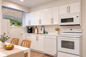 A modern kitchen with white cabinets, a microwave, an oven, and a coffee maker. - Boho 2BR | Monthly Stays | Quiet East Ottawa (Ottawa)