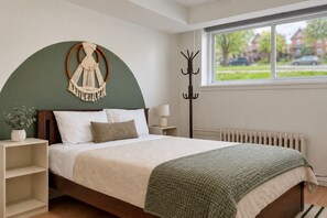 A bedroom with a bed, bedside tables, a coat rack, a window with a view, and a radiator. - Boho 2BR | Monthly Stays | Quiet East Ottawa (Ottawa)