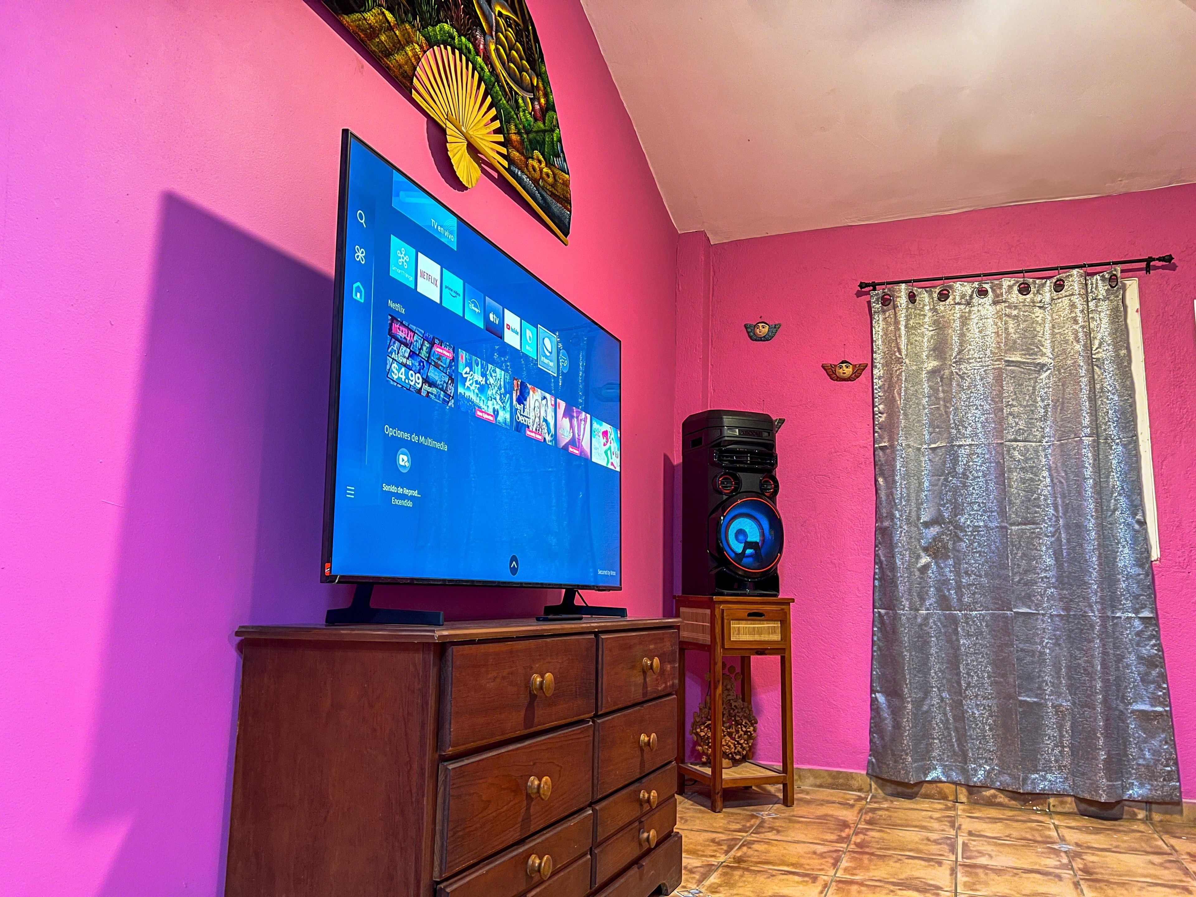 Una habitación con una televisión de pantalla plana montada en la pared, un aparador de madera y un altavoz sobre una mesita.