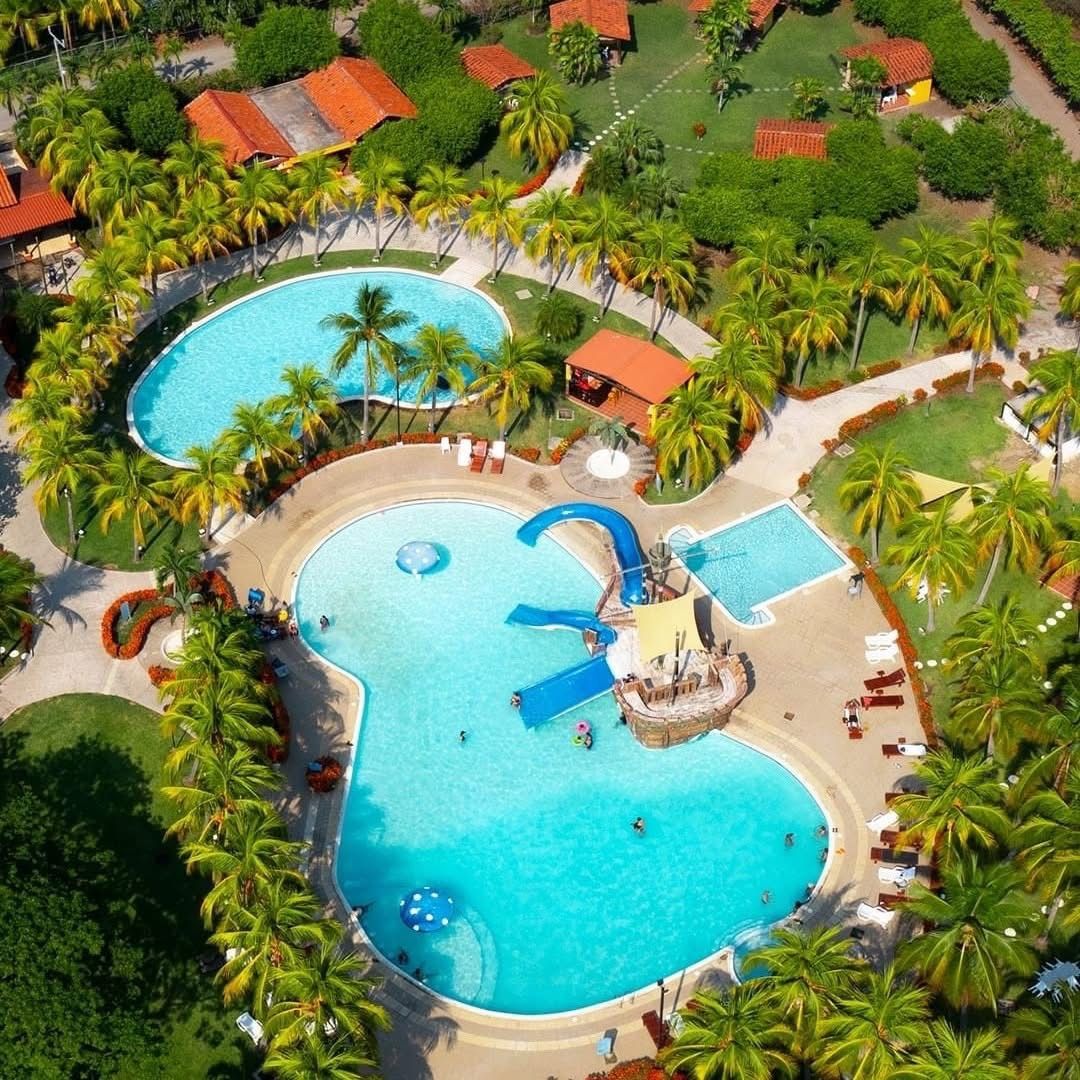 Un resort con dos piscinas grandes, palmeras y un tobogán de agua.