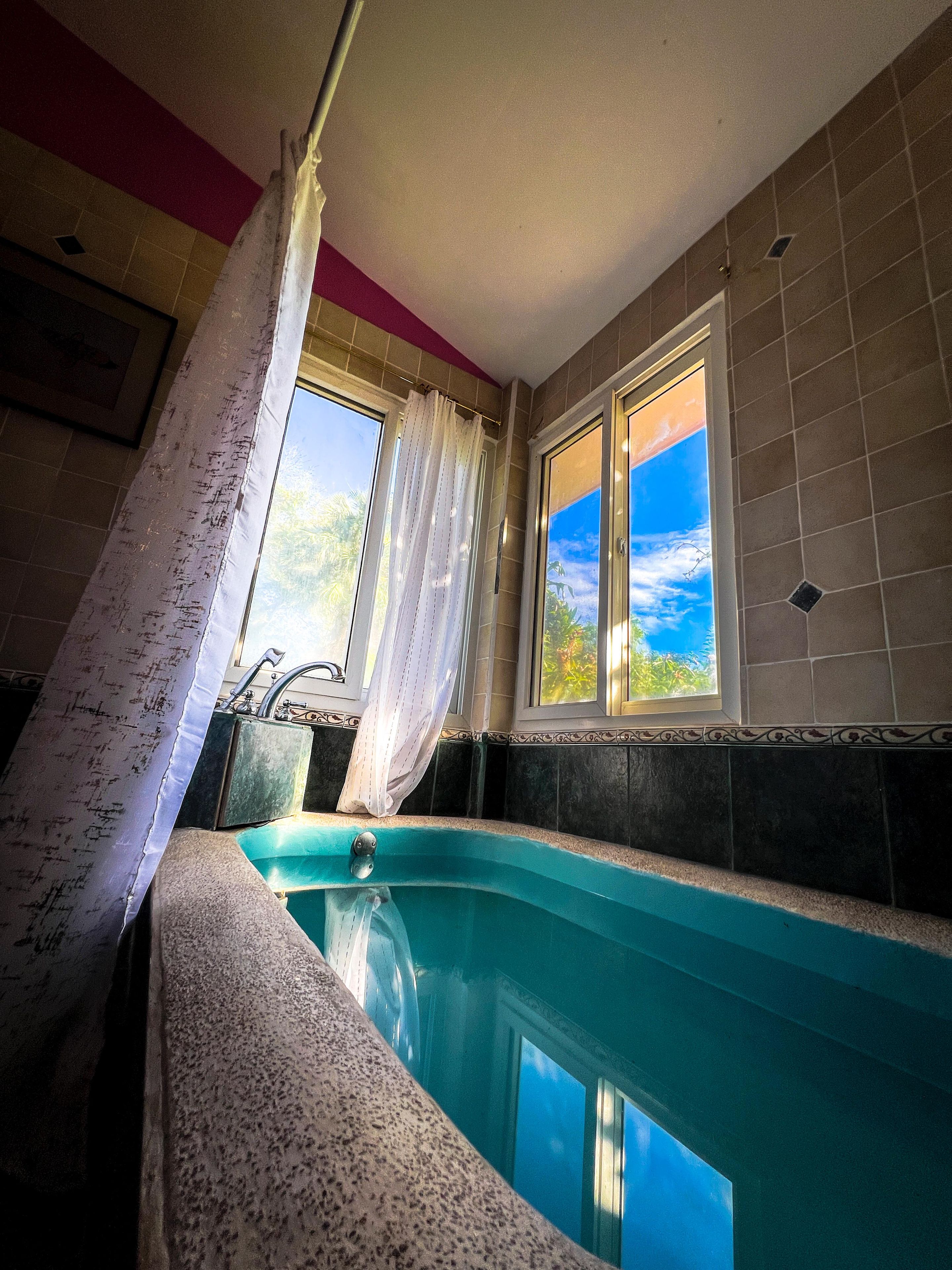 A spa area with a hot tub, a window with curtains, and a view of the sky.