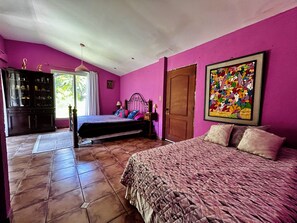 A bedroom with two beds, a wooden wardrobe, and a colorful painting on the wall. - Rancho Colibrí (Acajutla)