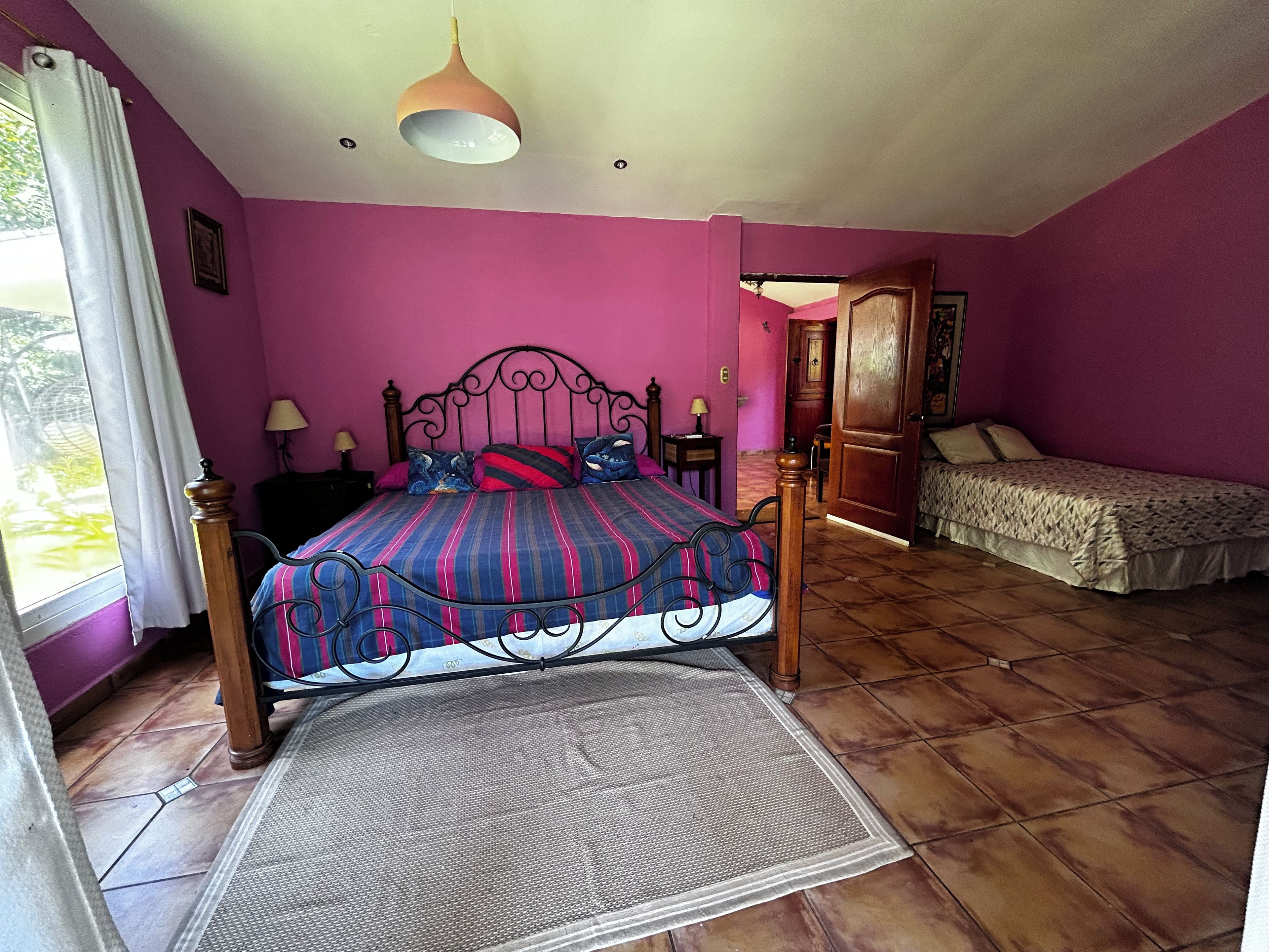 Un dormitorio con una cama, una cama adicional, una ventana con cortinas, una puerta y una lámpara colgante.