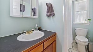 Een badkamer met een wit wastafel, een spiegel, een toilet en een douchegordijn.