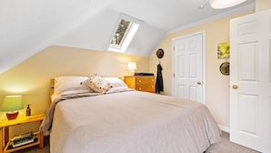 Een slaapkamer met een bed, nachtkastje, lamp, kapstok en een deur.