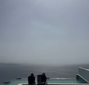 Blick von einem Infinity-Pool auf das Meer, zwei Personen sind sitzend zu sehen.