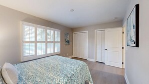 A bedroom with a bed, a large window with blinds, a closet, and a painting on the wall. - New to VRBO, 5BR Palmetto Dunes, 7.5 Min Walk To Beach, Private Pool (Hilton Head Island)