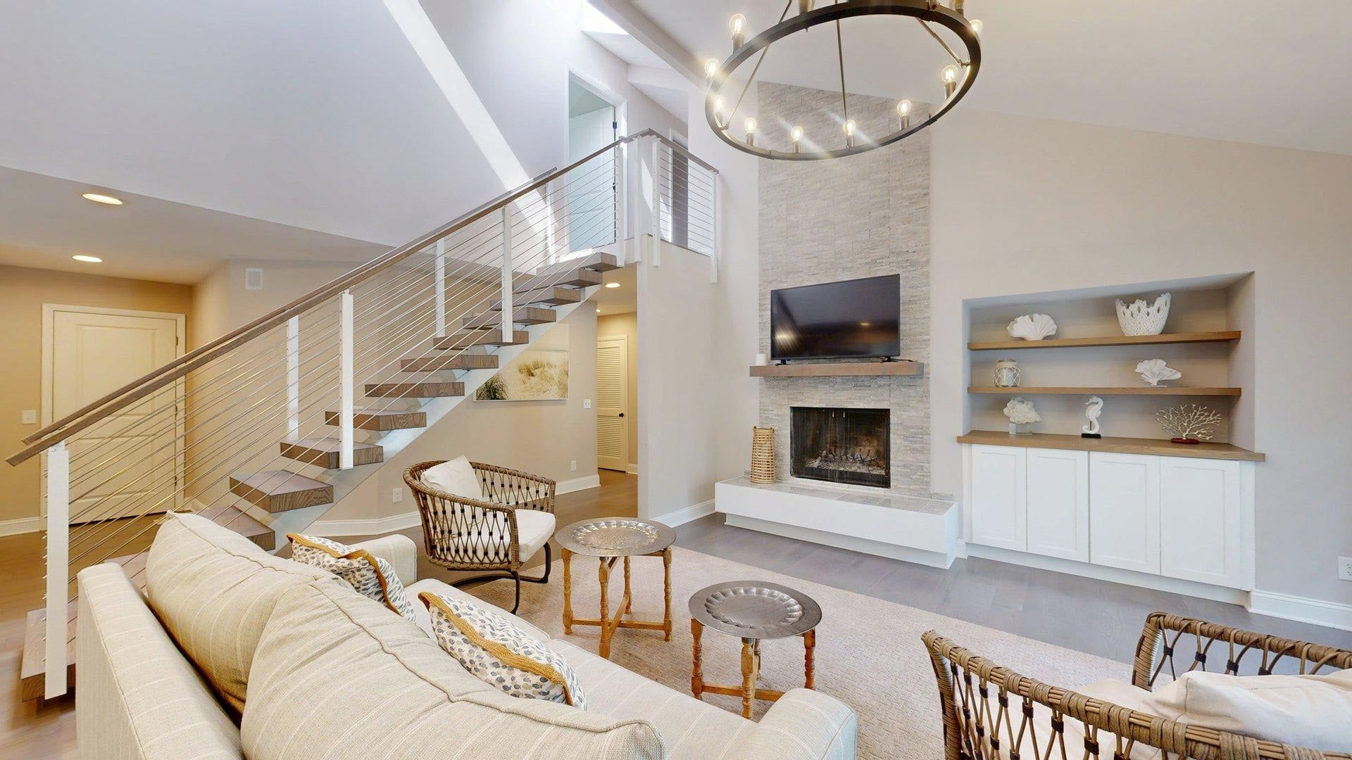 A modern living room with a staircase, a fireplace, and a flat-screen TV mounted above it.