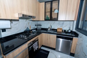 A modern kitchen with wooden cabinets, a black countertop, stainless steel appliances, and a marble backsplash. - Amazing 3-bedroom apartment with AC in charming Tangier (Tangier)