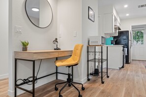 Una cocina moderna con encimera de madera, una silla de oficina amarilla, un espejo redondo y una isla de cocina con microondas y cafetera.
