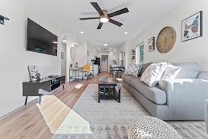 A modern living room with a sofa, coffee table, TV, and a ceiling fan. - F1 Ready - Heart of South Austin - 2B/1.25BA - King Bed - Fast WiFi - Yard (Austin)