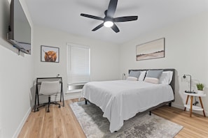 A bedroom with a bed, a desk, a chair, a ceiling fan, a window with blinds, and a wall-mounted TV. - F1 Ready - Heart of South Austin - 2B/1.25BA - King Bed - Fast WiFi - Yard (Austin)