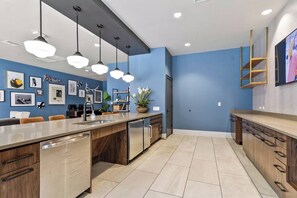 A modern kitchen with a central island, pendant lighting, and a blue accent wall. - The Whitmore Tuscaloosa • 1st Floor • 3BR/3BA • 1 Mile to UA (Tuscaloosa)