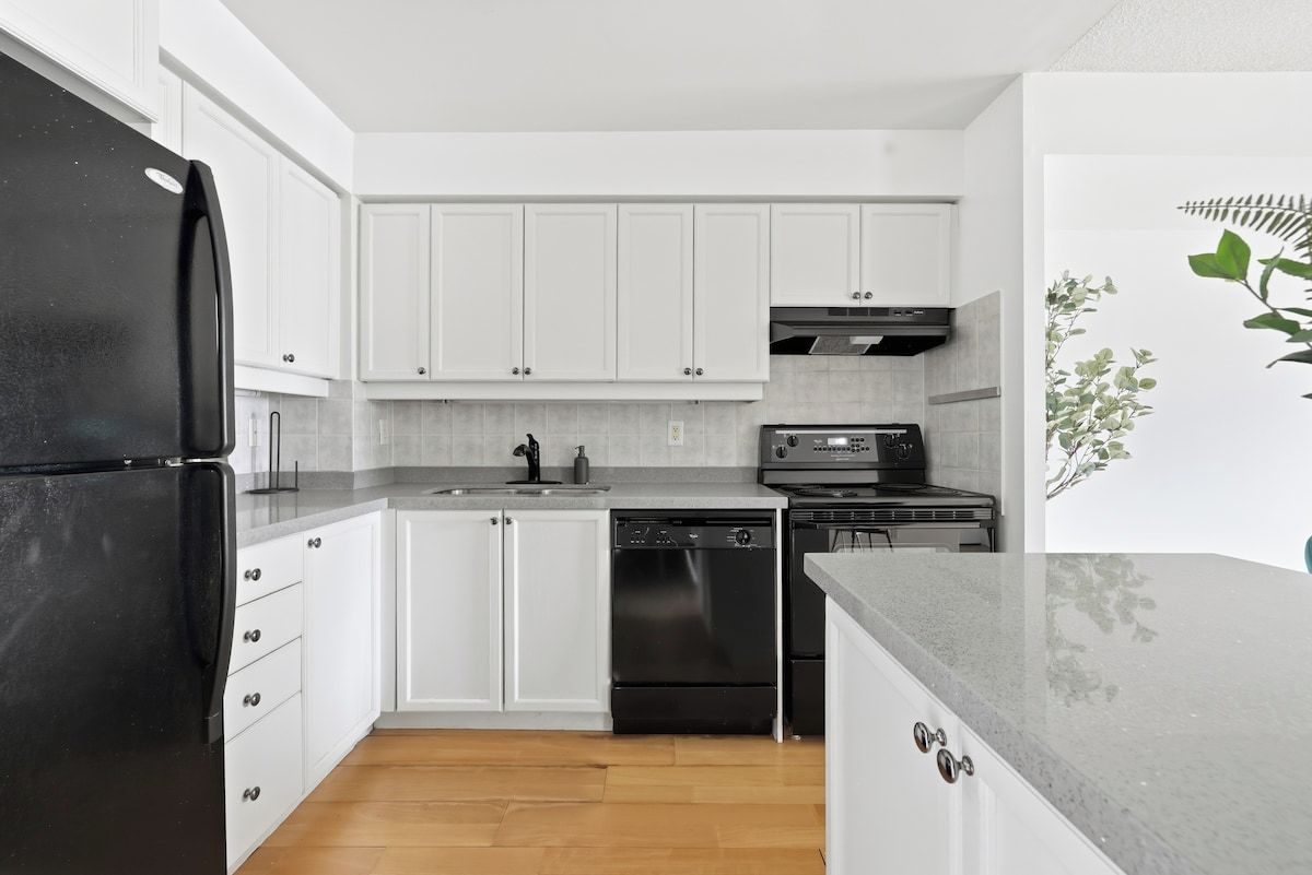 A modern kitchen with white cabinets, a black refrigerator, a dishwasher, and a built-in oven.
