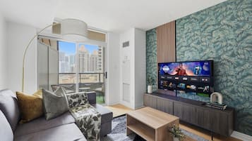 Una sala de estar moderna con un sofá, una mesa de centro y un televisor de pantalla plana montado en una pared con un papel tapiz con estampado de hojas.