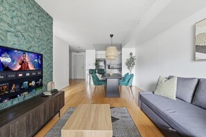 Una sala moderna con una televisión de pantalla plana, un sofá gris y un comedor con sillas color turquesa.
