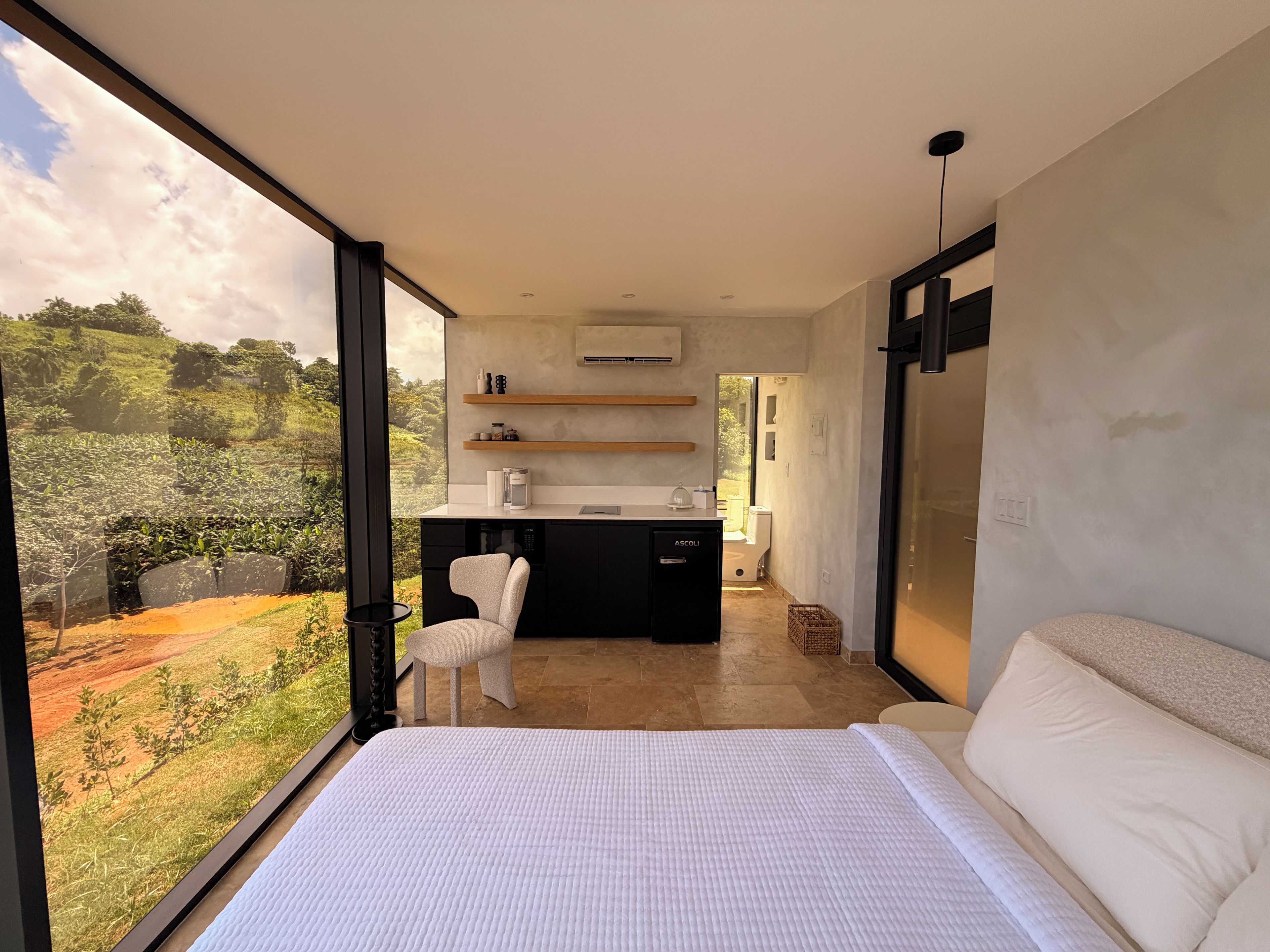 Une chambre moderne avec un grand lit, une vue sur l’extérieur, un petit coin cuisine et un fauteuil.